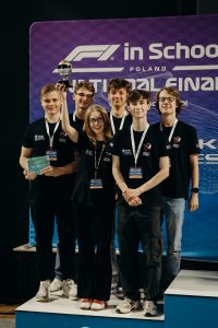 Grupa uczniów z medalami i pucharem na podium  po zdobyciu wice Mistrzostwa Polski w konkursie Formuły 1